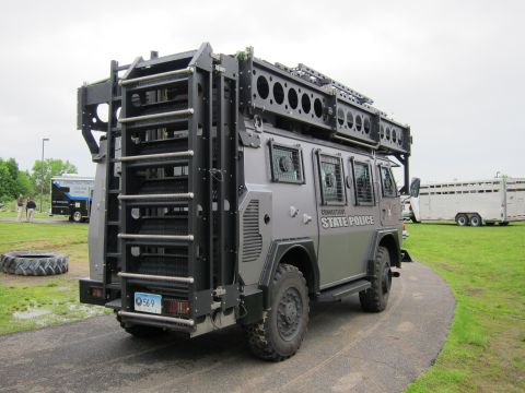 1991 Ford LTD Crown Victoria - Rear three-quarter view of a gray Connecticut State Police armored tactical truck with roof equipment and barred windows, parked on grass.