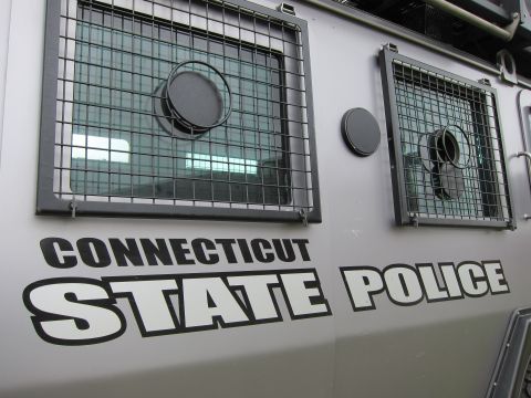 1991 Ford LTD Crown Victoria - Close-up of the side of a gray armored vehicle bearing CONNECTICUT STATE POLICE lettering and two barred windows.