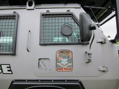 1991 Ford LTD Crown Victoria - Side of a gray armored vehicle showing a barred window, folding mirror, and a Connecticut State Police 1903 shield decal.