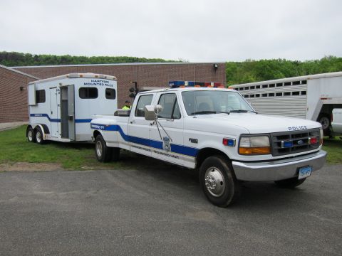 1991 Ford LTD Crown Victoria - white Ford crew-cab dually police pickup hitched to a Hartford Mounted Police horse trailer in front of a brick building.