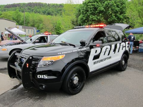 1991 Ford LTD Crown Victoria - Front three-quarter view of a black and white Ford Police Interceptor Utility SUV with brush guard and roof light bar at an outdoor event.
