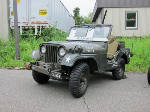 1991 Ford LTD Crown Victoria - olive-drab military jeep lettered US ARMY MILITARY POLICE with white star and unit markings, parked beside a trailer.