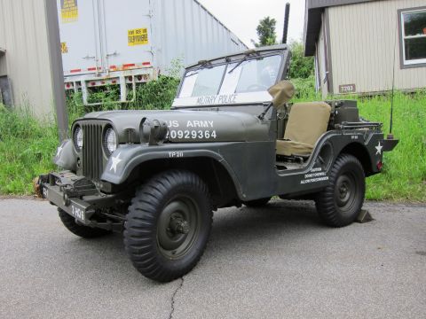 1991 Ford LTD Crown Victoria - Front three-quarter view of an olive-drab US Army Military Police jeep with white star, parked near a storage trailer.
