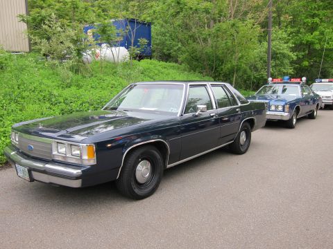 1991 Ford LTD Crown Victoria - dark blue Ford LTD Crown Victoria sedan parked on pavement, with state police cars visible behind it.