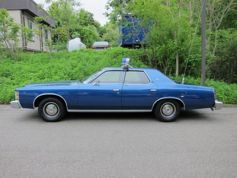 1991 Ford LTD Crown Victoria - Side profile of a blue Ford LTD four-door sedan with a single blue roof beacon, parked in front of greenery.