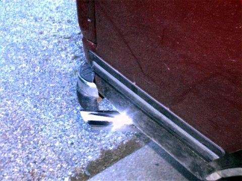 1990 Ford Bronco - The rear corner of a dark red vehicle is shown, with a chrome exhaust pipe visible.