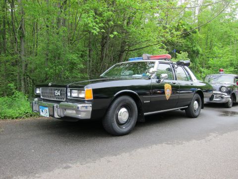 1991 Ford LTD Crown Victoria - Front three-quarter view of a black Chevrolet Caprice police sedan numbered 154 with gold door shield and roof lightbar.