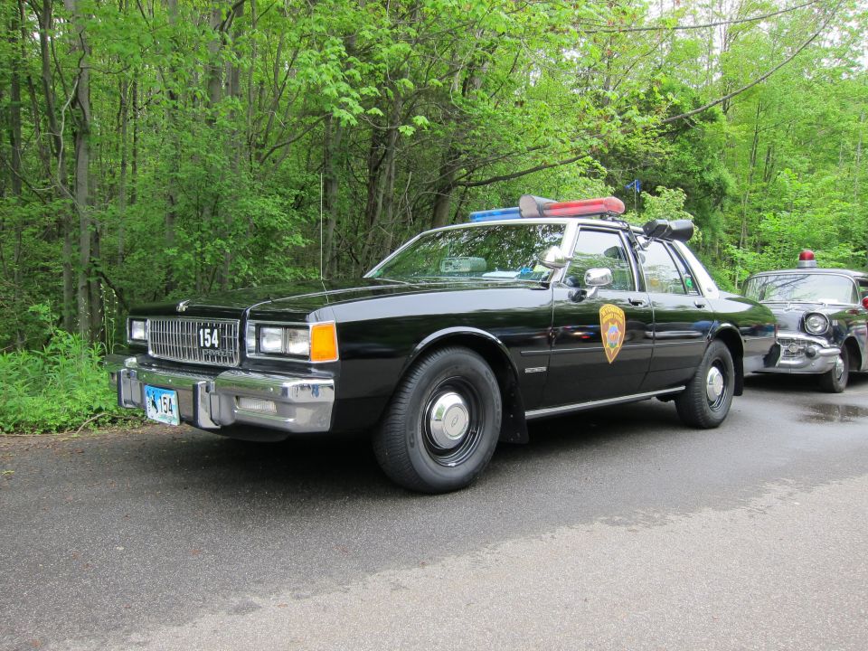 Front three-quarter view of a black Chevrolet Caprice police sedan numbered 154
