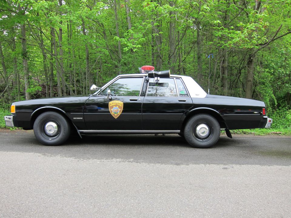 Side profile of a black and white Chevrolet Caprice police sedan with gold door shield
