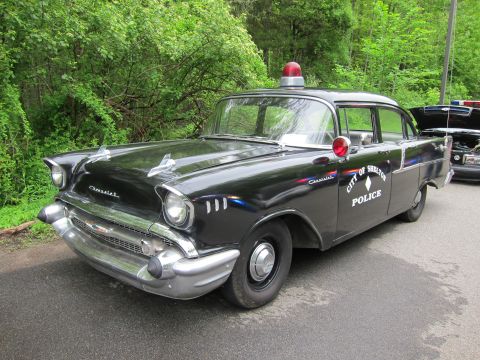 1991 Ford LTD Crown Victoria - Front three-quarter view of a black 1957 Chevrolet police sedan lettered CITY OF SHELTON POLICE with red roof beacon.