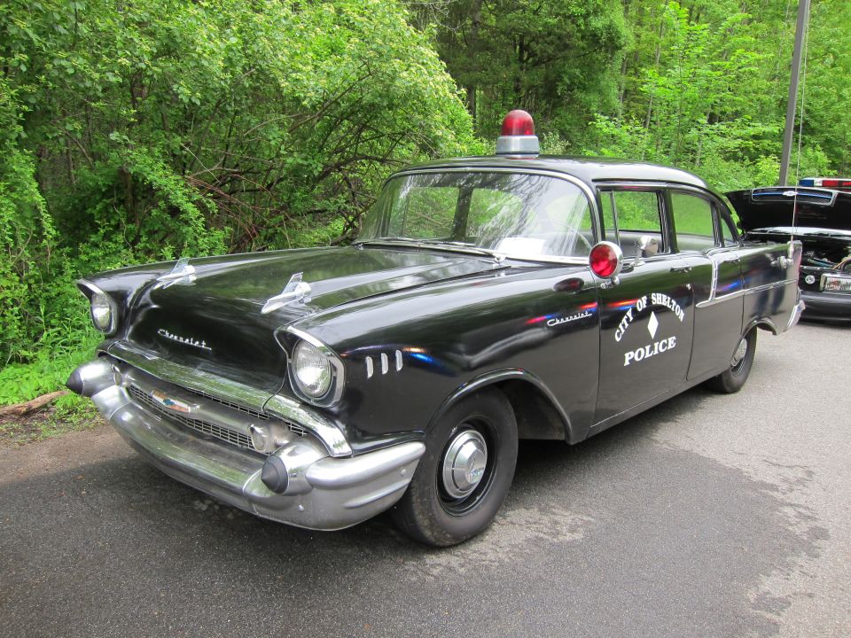 Front three-quarter view of a black 1957 Chevrolet police car marked CITY OF SHELTON
