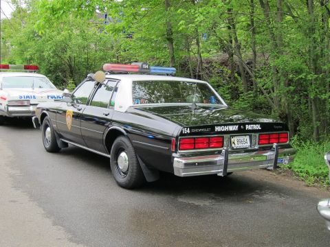 1991 Ford LTD Crown Victoria - black-and-white Chevrolet Caprice marked unit 154 Highway Patrol parked on a wooded roadside with light bar on roof.