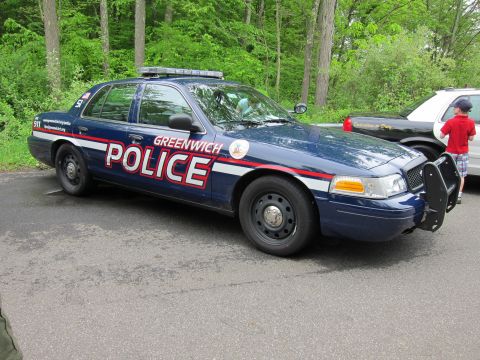 1991 Ford LTD Crown Victoria - dark blue Greenwich Police Ford Crown Victoria with red striping and push bar parked at a wooded lot, a child nearby.