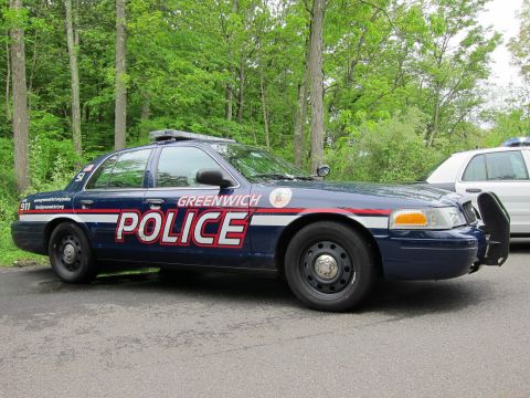 1991 Ford LTD Crown Victoria - Left side view of a dark blue Greenwich Police Ford Crown Victoria with roof light bar parked on pavement near woods.