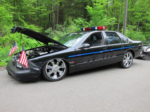 1991 Ford LTD Crown Victoria - lowered black Chevrolet Impala SS with hood raised, chrome wheels, roof light bar and small American flags on the front bumper.