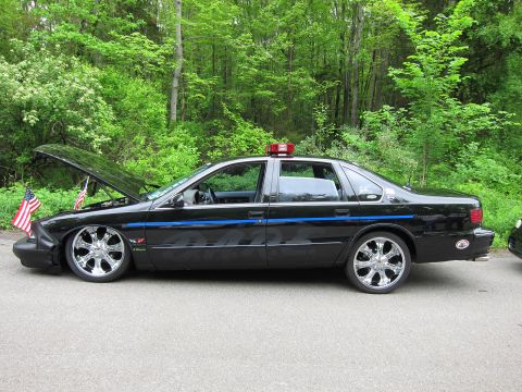 1991 Ford LTD Crown Victoria - Side profile of a lowered black Chevrolet Impala SS on large chrome wheels with hood open and a roof beacon.