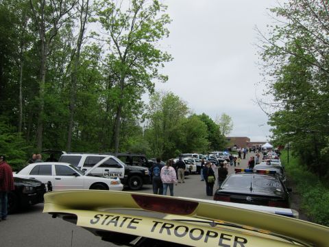 1991 Ford LTD Crown Victoria - Crowds and rows of parked police cars at an outdoor event, viewed past a yellow trunk lid lettered State Trooper.