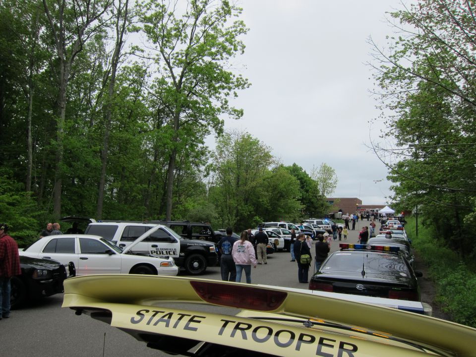 Crowd of people and parked police cars at an outdoor car show