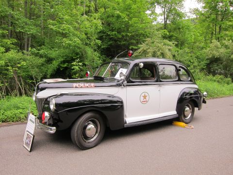 1991 Ford LTD Crown Victoria - restored black-and-white vintage police sedan lettered POLICE with a roof beacon and star door emblem, with display placard.