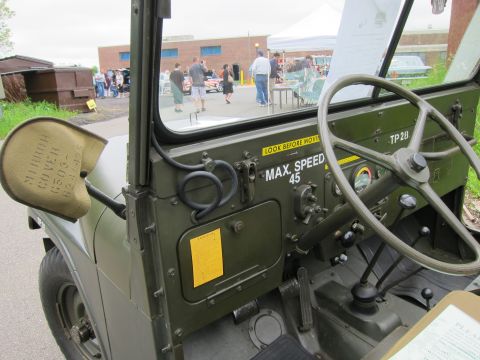 1991 Ford LTD Crown Victoria - Close view of an olive-drab military jeep's dash and side mirror stenciled MAX SPEED 45 and TP 28, with event crowd beyond windshield.