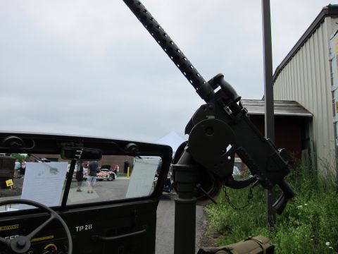 1991 Ford LTD Crown Victoria - belt-fed .50 caliber machine gun mounted on an olive-drab military jeep, aimed skyward against an overcast sky and metal building.