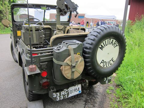 1991 Ford LTD Crown Victoria - Rear view of an olive-drab military jeep with jerry can, mounted gun and spare tire cover lettered MILITARY POLICE.