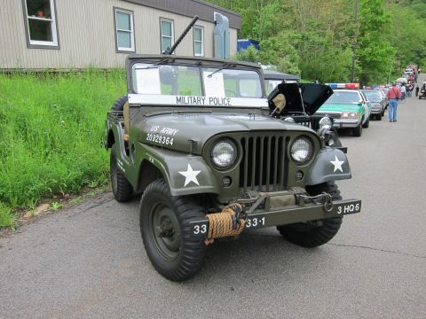 1991 Ford LTD Crown Victoria - Front three-quarter view of an olive-drab US Army Military Police jeep with mounted gun and winch, parked near a building.