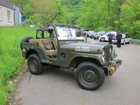 1991 Ford LTD Crown Victoria - Side view of an olive-drab US Army jeep stenciled 20929364 with mounted gun and front winch, parked beside other cars.