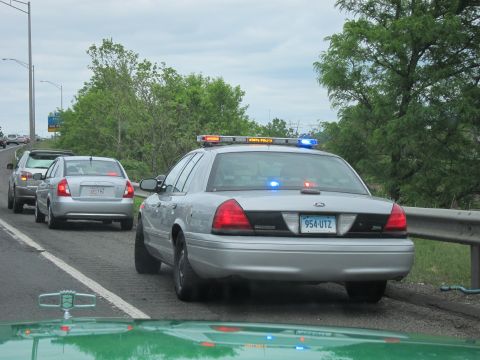 1991 Ford LTD Crown Victoria - silver Ford Crown Victoria state police car with activated lights stopped behind a silver sedan on a highway shoulder.