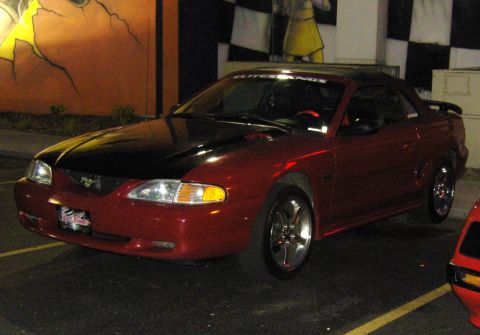 2007 Ford Mustang - Red convertible with black hood and spoiler parked at night, with another car partially visible.