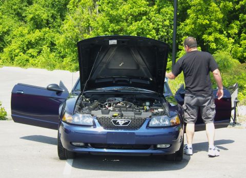 2007 Ford Mustang - Man inspects the engine of a blue Ford Mustang with its hood and doors open.