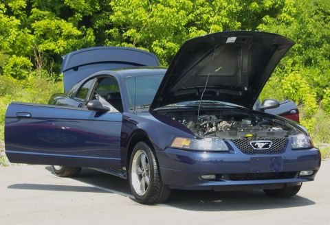 2007 Ford Mustang - A blue Ford Mustang is parked outside with its hood and driver's door open, revealing the engine bay.