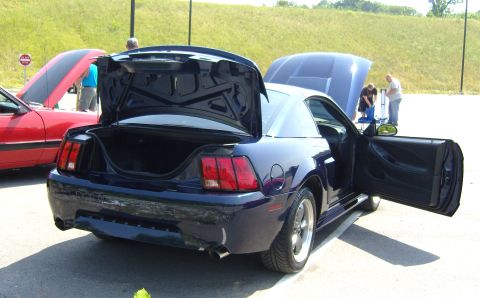 2007 Ford Mustang - Dark blue Ford Mustang from the early 2000s, trunk and door open, parked next to a red car.