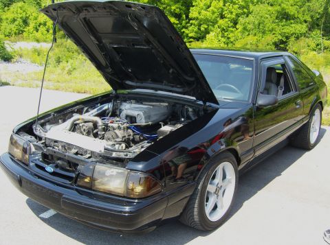 2007 Ford Mustang - Black Ford Mustang with hood open, displaying its engine bay. Fox body style is evident.