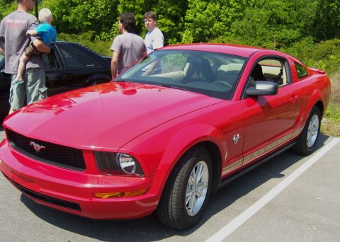 2007 Ford Mustang - A red Ford Mustang is parked in a lot with people nearby.