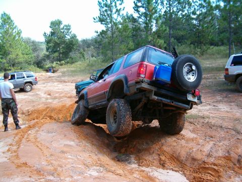 1991 Ford Bronco - Multiple SUVs tackle a challenging off-road course with steep inclines and sandy terrain.