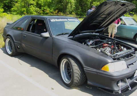 2007 Ford Mustang - A matte black Ford Mustang is displayed with its hood open, revealing the engine bay and interior roll cage.
