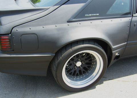 2007 Ford Mustang - Close-up of a modified Ford Mustang's rear quarter panel and wheel, showing custom fender flares and a black mesh wheel.