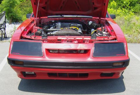 2007 Ford Mustang - The engine bay of a red Ford Mustang is visible with the hood open, revealing the motor and surrounding components.