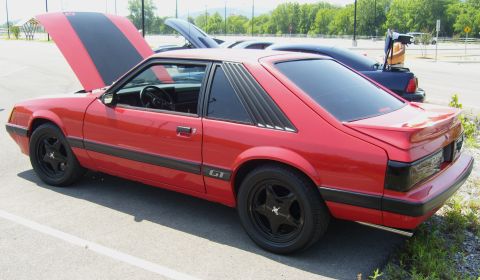 2007 Ford Mustang - A red Ford Mustang GT with its hood open and black racing stripes is parked next to another car.