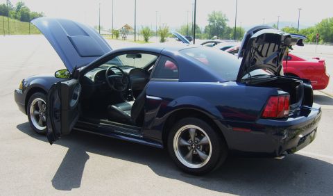 2007 Ford Mustang - A dark blue 2007 Ford Mustang is displayed with its hood and trunk open, parked in an outdoor lot with other vehicles visible.