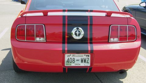 2007 Ford Mustang - The rear of a red Ford Mustang is visible, black racing stripes and a spoiler.