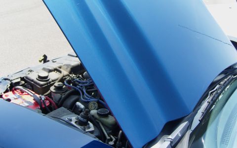 2007 Ford Mustang - Engine bay of a blue vehicle, with the hood raised to reveal the engine and battery. No specific year is discernible from the visible parts.