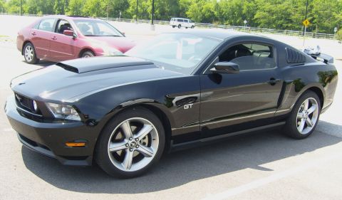 2007 Ford Mustang - A black 2007 Ford Mustang GT is parked in a lot, showing its distinctive hood scoop and GT badging.