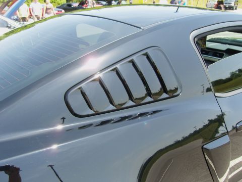 2007 Ford Mustang - A black coupe's side window louvers are visible, with other vehicles and people in the background.