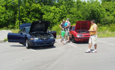 2007 Ford Mustang - Two cars are parked with their hoods open, while people gather around them on a sunny day.