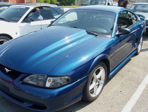 2007 Ford Mustang - Blue coupe with a prominent hood scoop is parked next to a white convertible.