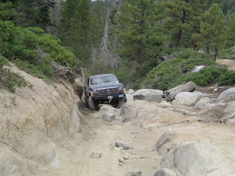 1985 Ford Bronco - This truck is navigating a challenging off-road trail with steep inclines and large boulders.