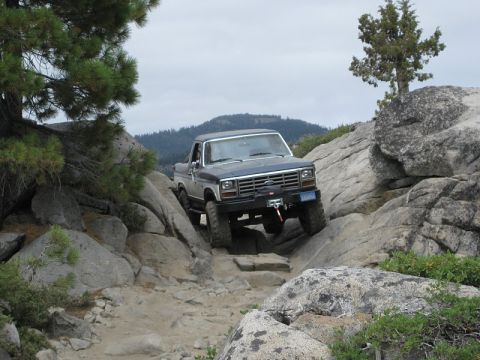 1985 Ford Bronco - Ford Bronco tackling a challenging off-road course in a mountainous, wooded area.