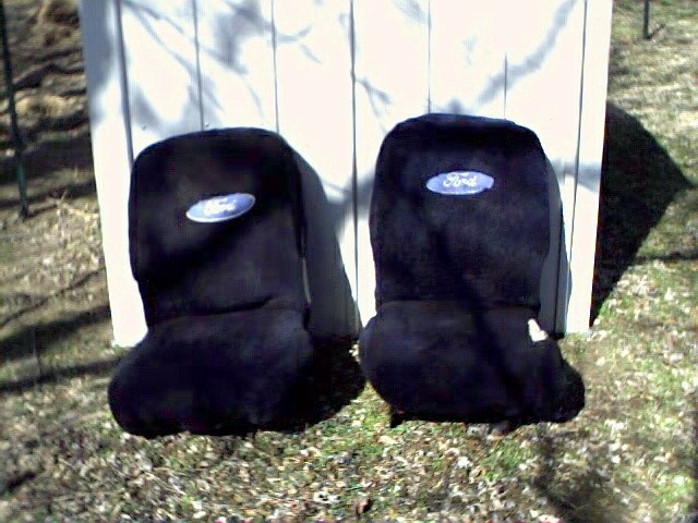 Pair of black bucket seats with Ford-logo covers set on grass by a white fence